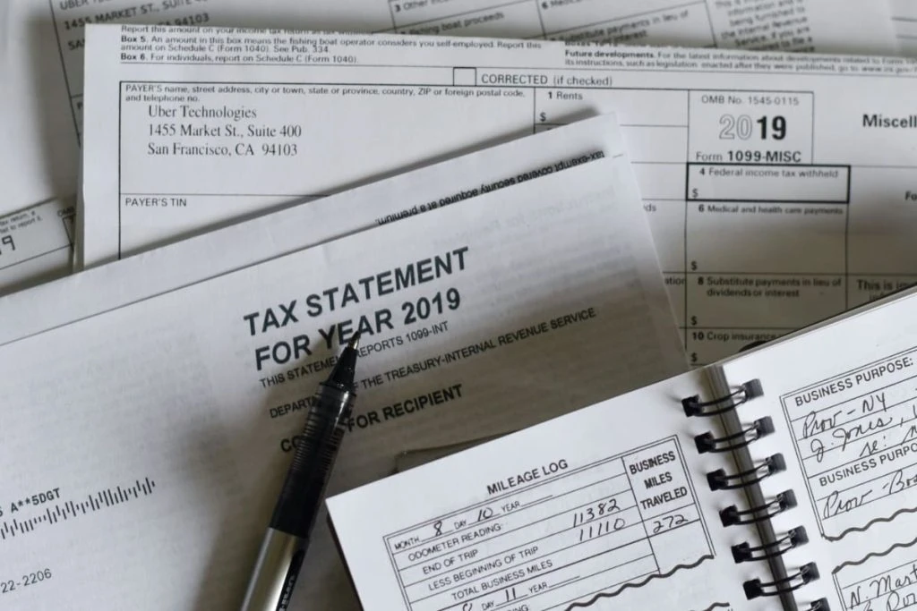 A stack of tax forms and a pen on a table.