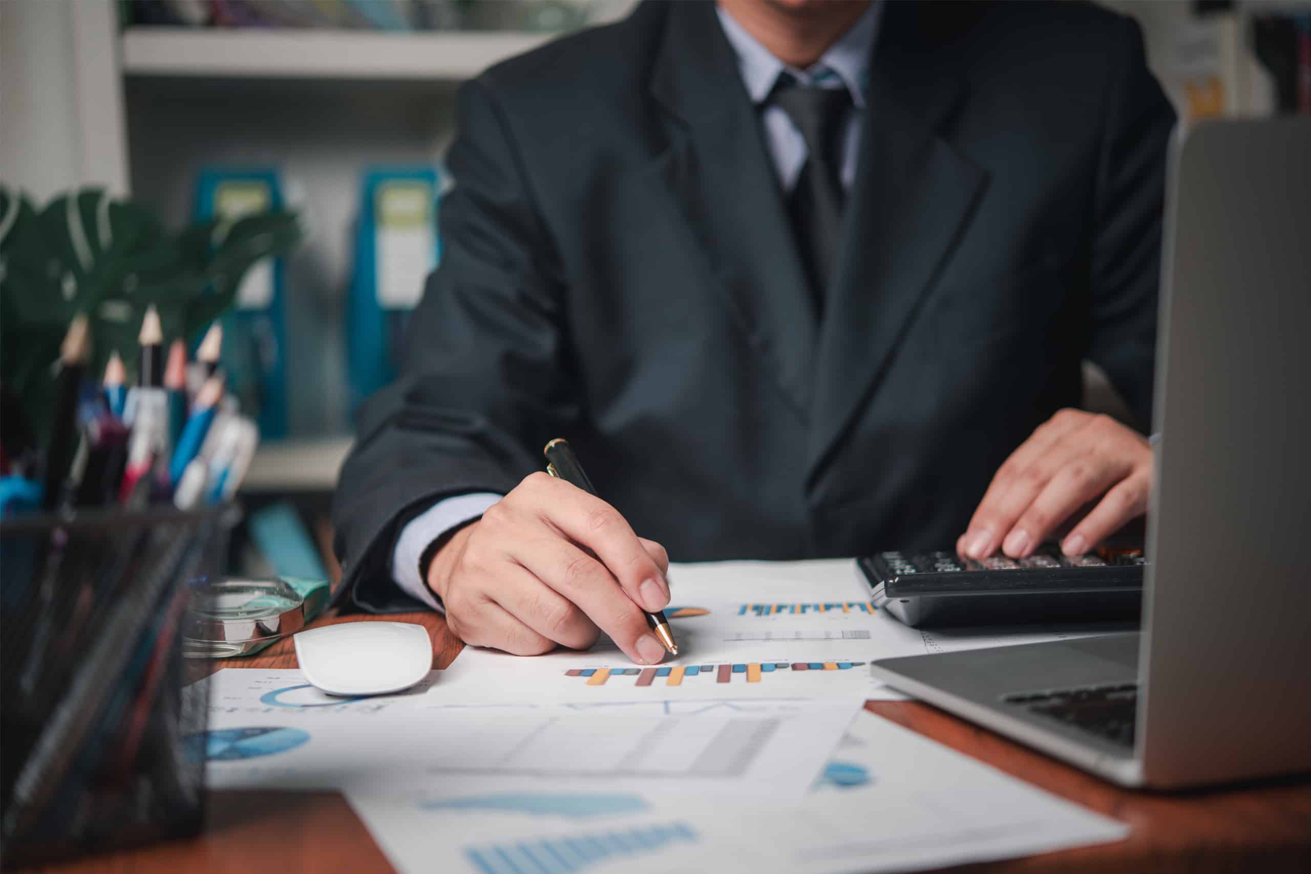 A chartered accountant in Ottawa is working diligently at a desk with documents containing charts and graphs, using a calculator, with a laptop nearby.