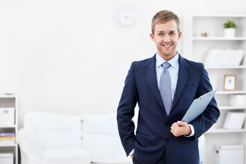 A smiling businessman, who is also a Tax Preparer, holding a clipboard in an office.