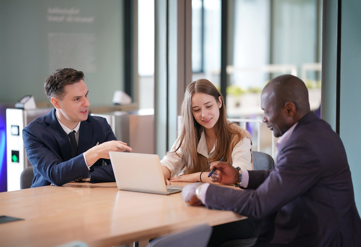 Three people are seated at a table in an office, engaged in a discussion. One person, a tax accountant in Ottawa, is pointing at a laptop while the others listen and smile.