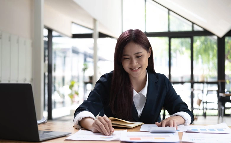 A Chartered Accountant in Ottawa sits at a desk, working with documents and charts, with a laptop open beside her in a bright, modern office.