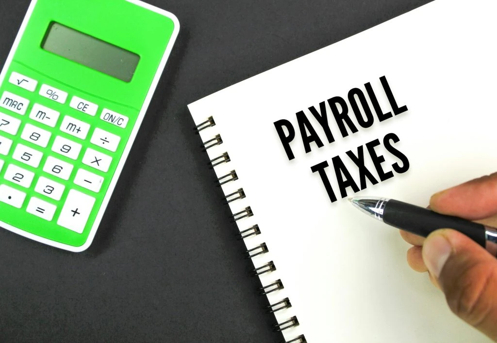 A person holds a pen next to a spiral notebook with "PAYROLL TAXES" written on it. A green calculator and a brochure for Tax Services in Ottawa are on the left.