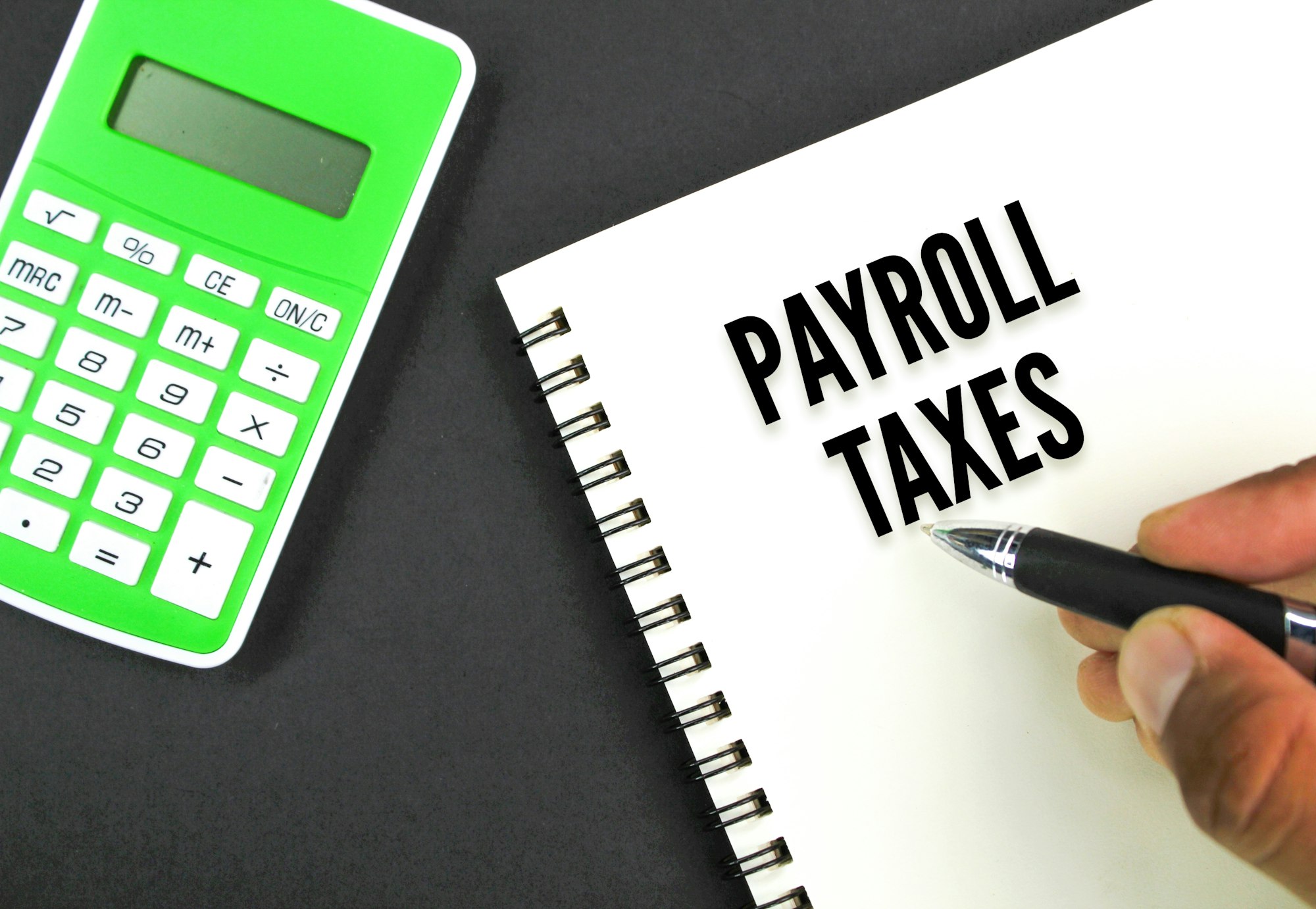 A person holds a pen next to a spiral notebook with "PAYROLL TAXES" written on it. A green calculator and a brochure for Tax Services Ottawa are on the left.