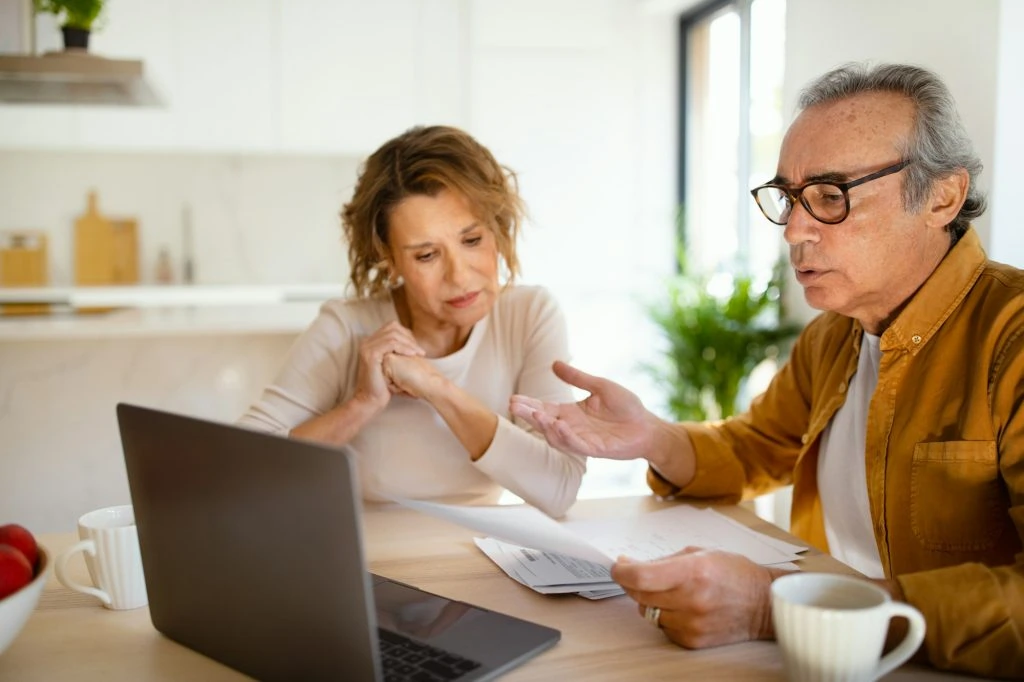 Two elderly individuals sit at a table, looking at a laptop and discussing documents with their tax accountant in Ottawa in a bright, modern kitchen.