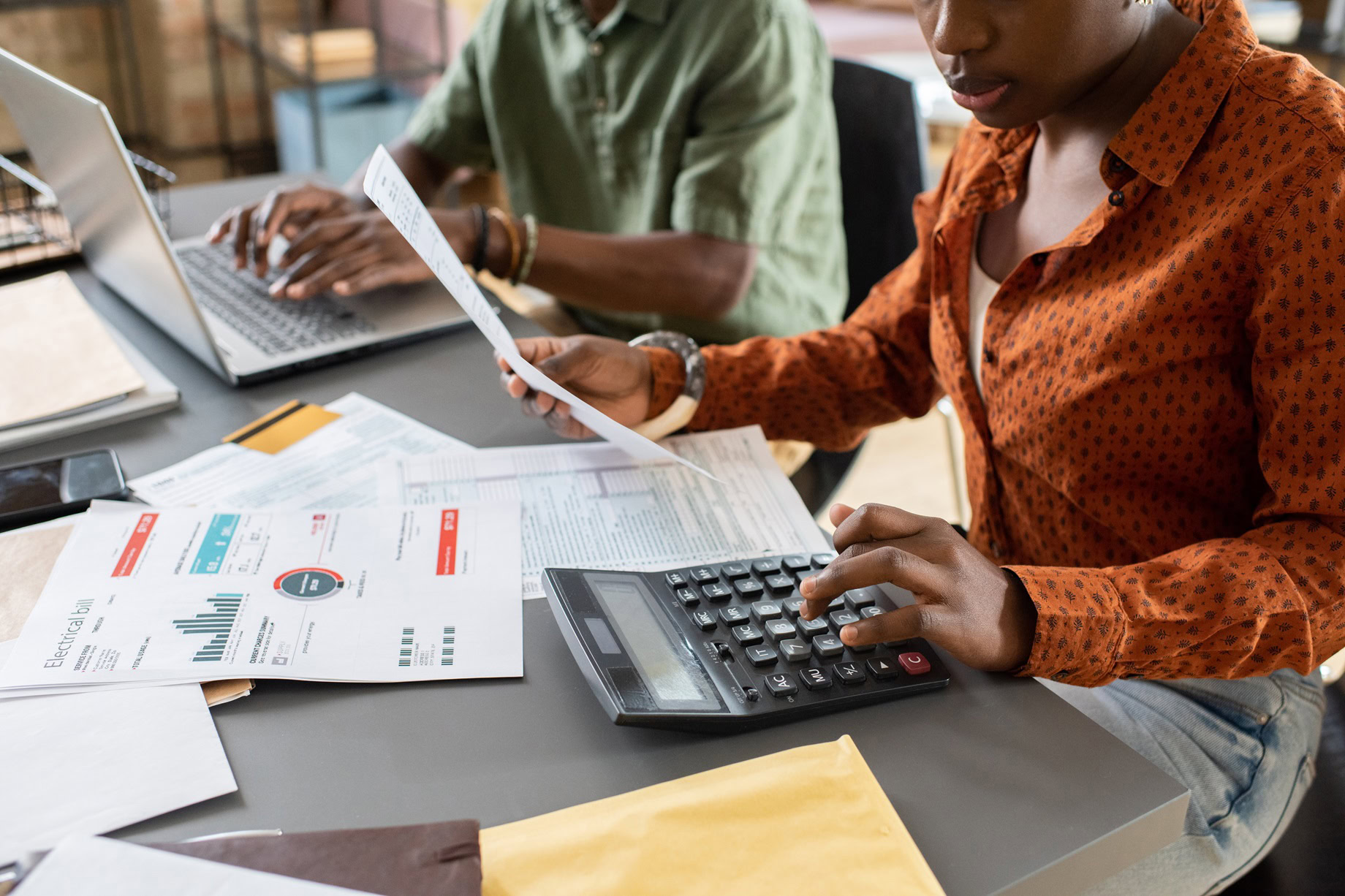Two people collaborate at a table with a laptop, documents, and a calculator. One is typing diligently, while the other reviews charts on a paper using the calculator. Their focused work exemplifies top-tier tax services in Ottawa.